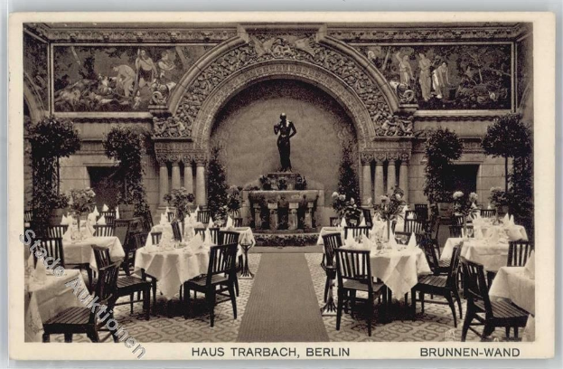 Ein altes Schwarz-Weiß-Foto eines Restaurants in Berlin, Deutschland, mit Tischen und Stühlen mit Blumenvasen, einer Statue im Hintergrund und Skulpturen und Pflanzen an den Wänden, mit Text am unteren Bildrand.