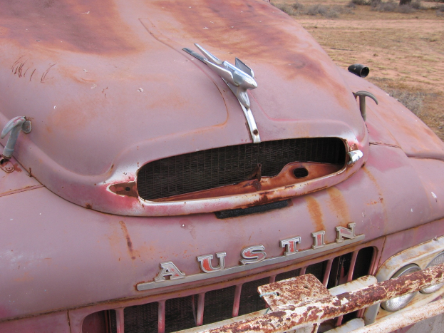 Alter rostiger Laster auf einem Feld mit Bäumen und einem klaren blauen Himmel, der Spuren von langfristiger Witterungseinwirkung zeigt.