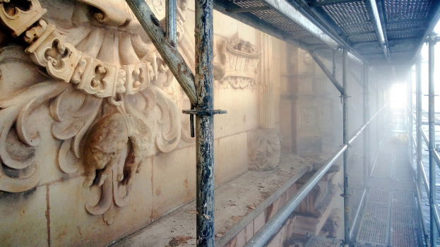 Ein renoviertes Gebäude mit detaillierten Schnitzereien an der linken Wand, Metallstangen auf der rechten Seite und einem Dach darüber.