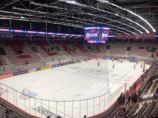 Eishockeyspiel in einer großen Arena zwischen den St. Louis Blues und Detroit Red Wings, mit Zuschauern auf den Sitzen und Stehplätzen in der Nähe des Spielfelds, umgeben von einem Zaun, einem Display, Metallrahmen, Deckenleuchten und einem Dach.