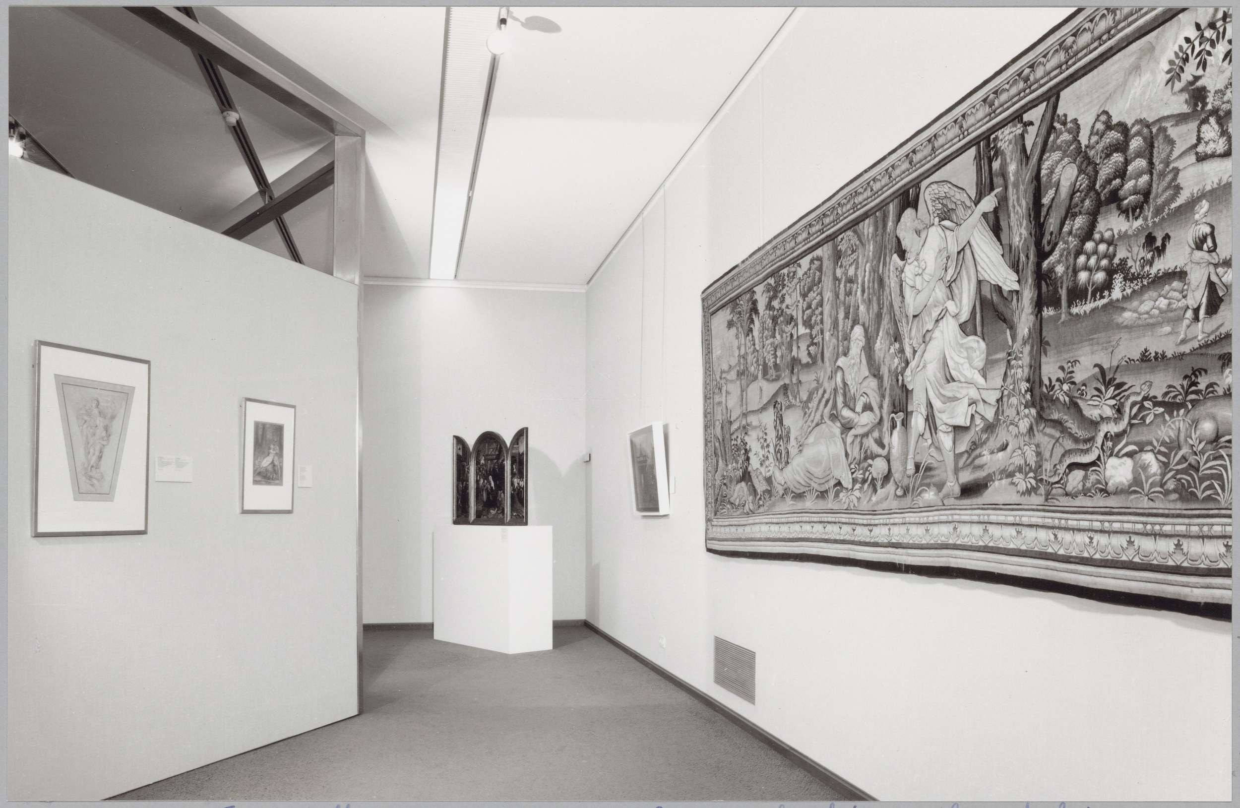 Schwarzes und weißes Foto einer Museumsgalerie mit einem großen Wandteppich, gerahmten Kunstwerken an den Wänden, auf einem Sockel montierten Objekten und Deckenleuchten, mit "Museum of Fine Arts, New York City" unten sichtbar.