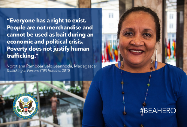 Frau in blauem Kleid vor einem Gebäude mit einem Zitat über Menschenhandel, lachend mit Menschen, Pflanzen und Flaggen im Hintergrund.