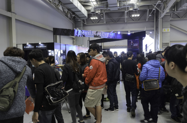 Eine Gruppe von Menschen vor einem vollen Gaming-Expo, mit Texttafeln, Deckenleuchten und Rohren im Hintergrund.