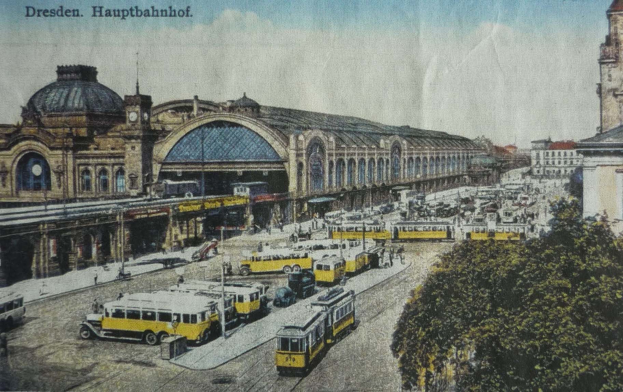 Schwarz-weiße Postkarte des Dresdner Hauptbahnhof Bahnhofs in Deutschland, die eine belebte StraßenSzene mit Fahrzeugen, Fußgängern, Bäumen, Gebäuden und einem bewölkten Himmel zeigt.