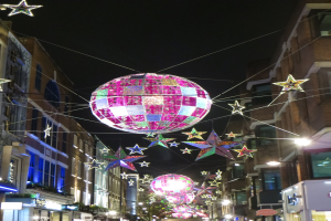 Eine festlich geschmückte Stadtstraße bei Nacht mit einem großen Diskokugel an einem Gebäude hängend und beleuchteten Dekorationen.