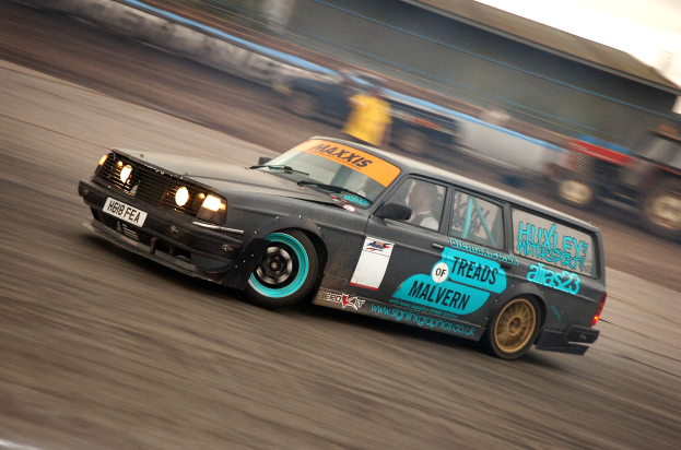Ein Auto fährt auf einer Rennstrecke, umgeben von anderen Fahrzeugen, mit einer Person darin, der Hintergrund ist unscharf durch die Bewegung.