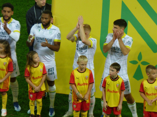 Eine Gruppe junger Fußballspieler in Uniformen klatscht feiernd auf einem Ligue-1-Feld, mit einem "Ligue 1"-Schild im Hintergrund.
