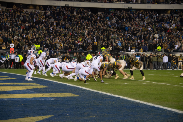 Fußballspieler in Sportkleidung und Helmen auf dem Boden liegend während eines Spiels in einem Stadion mit Zuschauern und Tafeln im Hintergrund.
