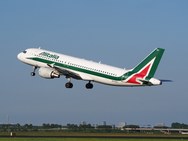 Ein Airbus A320-232 ERJ-EJZ der Alitalia startet vom Frankfurter Flughafen, mit grünem Gras, B├Ąumen, Geb├Ąuden und einem klaren blauen Himmel im Hintergrund.