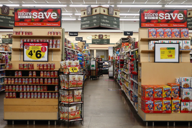 Ein Kiosk-Innenraum Mit Verschiedenen Lebensmitteln, Die Auf Regalen, Regalen Und Dem Boden Angezeigt Werden, Including Beleuchtete Schilder Mit Text Und Zahlen Und Deckeneinbauleuchten.