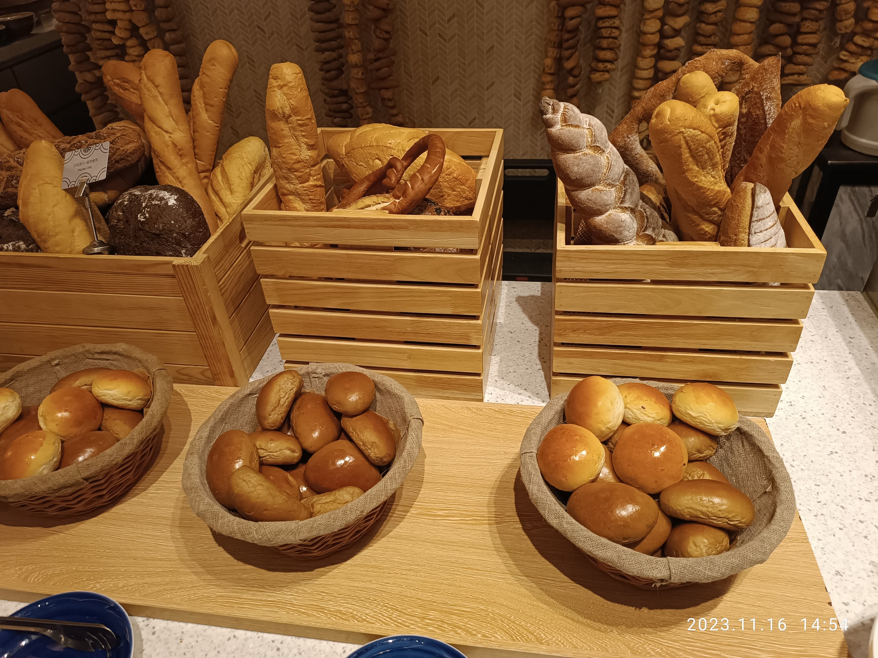 Holztisch mit Körben voller Brot, Tellern und Löffeln in einer Pariser Bäckerei mit einer gewässerten Wand.