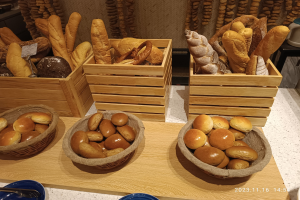 Holztisch mit Körben voller Brot, Tellern und Löffeln in einer Pariser Bäckerei mit einer gewässerten Wand.