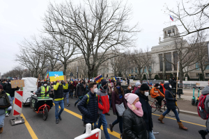 Eine große Gruppe von Menschen marschiert bei einer Demonstration in Washington, D.C. am 21. Januar 2020 die Straße entlang, mit Schildern und Bannern, einige fahren Fahrräder, es gibt auch Schilderstände, Bäume und einen klaren blauen Himmel im Hintergrund.