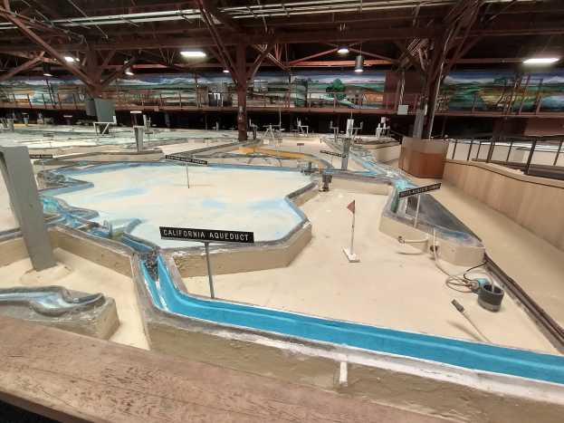 Ein großes Indoor-Wasserpark mit zahlreichen Wasserrutschen, Pfosten, Texttafeln, Deckenleuchten und Wandgemälde, das wie ein Minigolfplatz gestaltet ist.