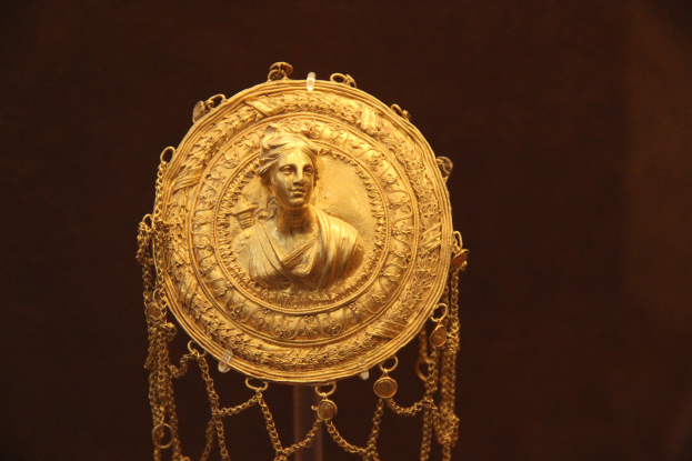 Goldene Medaille mit einer Frauengestalt, die detailliert verziert ist, vor dunklem Hintergrund.