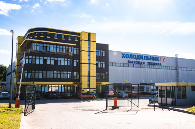 Großes Gebäude mit einem Metalltor, Straßenlaterne, Gras, Bäumen und einem bewölkten Himmel, das als Hauptquartier der russischen Automobilindustrie dient, mit einem Schild und vielen geparkten Autos davor.