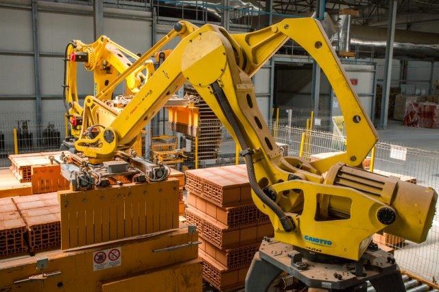 Großes Industrie-Lager mit gestapelten Kisten, Kränen, Zaun, Pfählen und einer fernen Wand in einer Fertigungsumgebung.