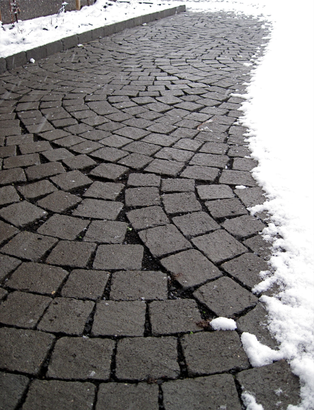 Eine Kopfsteinpflasterstraße mit leichtem Schnee bedeckt und ein Zaun im Hintergrund sichtbar.