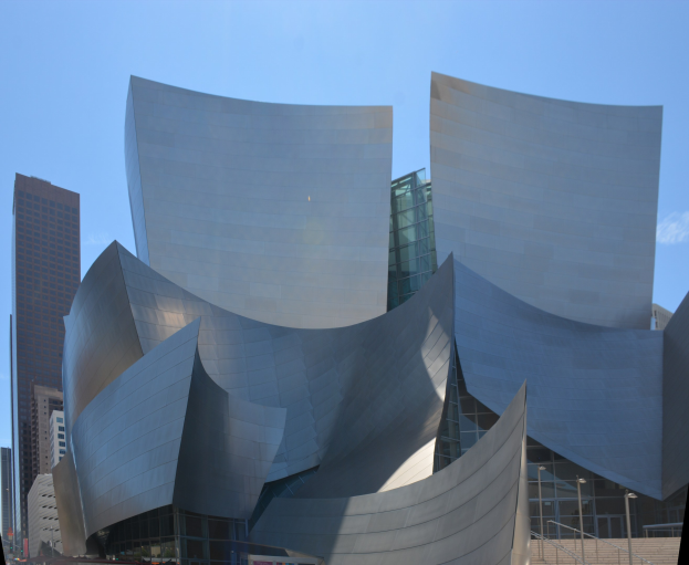 Modernes gläsernes Konzerthaus mit Treppen und Geländern zum Eingang, umgeben von Menschen, anderen Gebäuden und einem klaren blauen Himmel in Los Angeles.