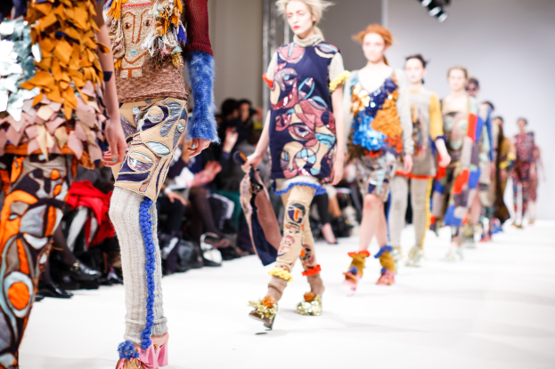 Eine Gruppe Von Frauen, Die Eine Laufsteg In London Fashion Week Mit Einem Publikum Im Hintergrund Unter Helllem Licht Gehen.
