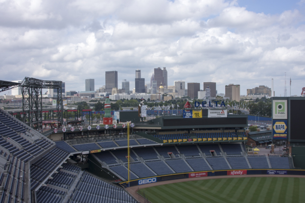 Ein Baseball-Stadion mit leeren Sitzplätzen, Pfählen und Beschriftungen, mit einem bewölkten Himmel und einer Stadt Silhouette im Hintergrund.
