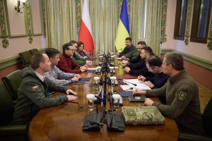 Eine Gruppe von Männern in einem offiziellen Setting mit Flaggen und Vorhängen im Hintergrund, die um einen Holztisch mit Mikrofonen und Dokumenten sitzen und eine intensive Diskussion führen.