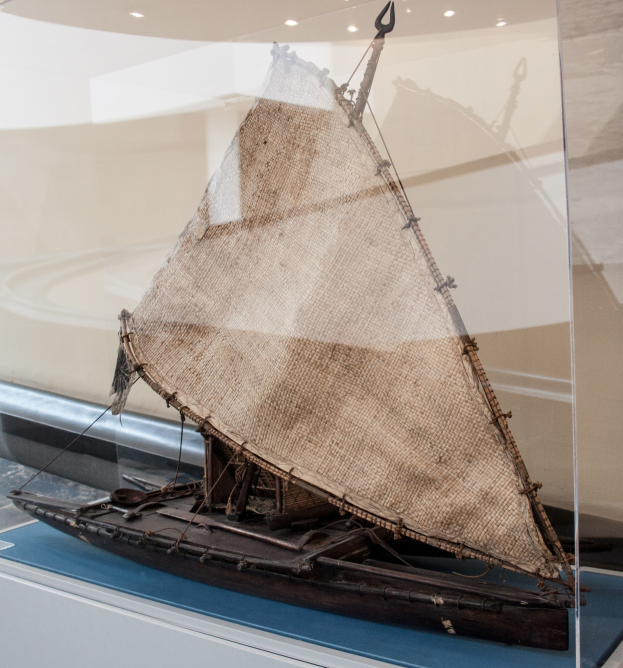 Ein Modellsegelboot mit geblähten Segeln, das in einer Glasvitrine ausgestellt ist und an einer Wand mit Deckenbeleuchtung steht.