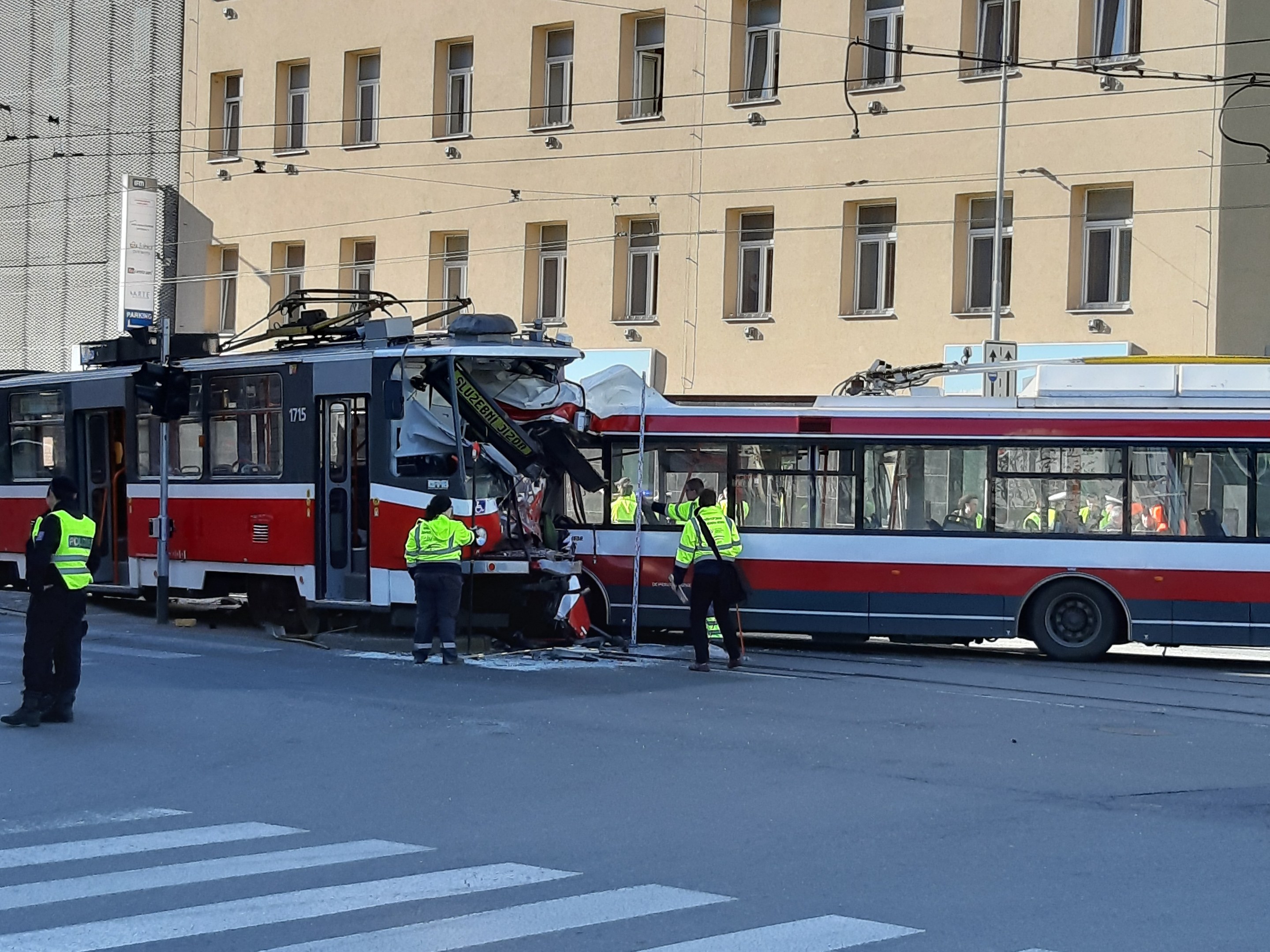 Eine rote und weiße Straßenbahn, die auf der Straße in einen Unfall verwickelt ist, mit ein paar Menschen in der Nähe und einem Gebäude im Hintergrund.