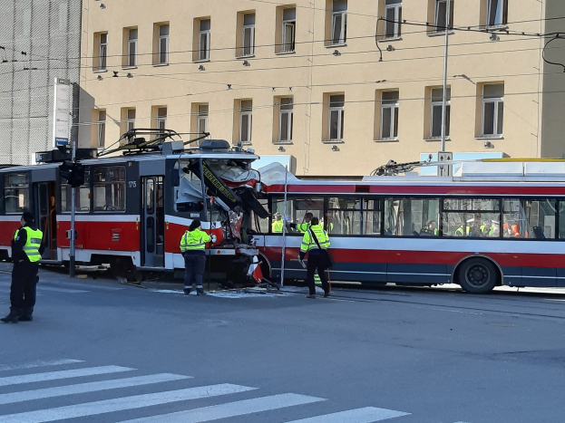 Eine rote und weiße Straßenbahn, die auf der Straße in einen Unfall verwickelt ist, mit ein paar Menschen in der Nähe und einem Gebäude im Hintergrund.