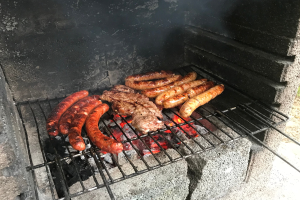 Grill mit Würstchen und Fleisch, das über Kohle und Flammen gegrillt wird, auf Gras im Freien