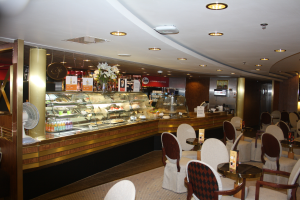 Ein Restaurant-Innenraum mit Tischen und Stühlen vor einer Theke, geschmückt mit Blumenvasen, Tafeln mit Text, einem Ventilator und anderen Gegenständen unter einer mit Lampen beleuchteten Decke.