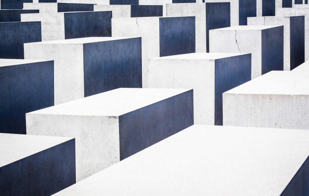 Luftaufnahme des Holocaust-Mahnmals für die ermordeten Juden Europas in Berlin, mit zahlreichen weißen und blauen Betonstelen in einem Gittermuster.