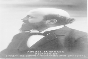 Schwarzes und weißes Foto von August Scharrer, einem deutschen Komponisten, der einen Blazer und eine Krawatte trägt, mit Text am unteren Bildrand.