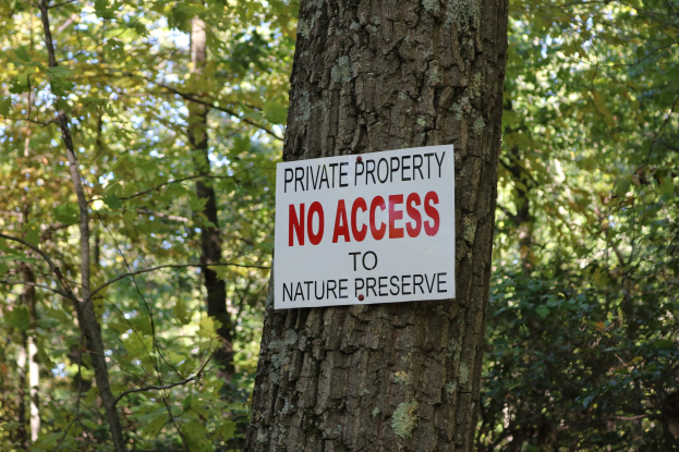Ein Baum mit einem "Privatgrundstück Kein Zugang zum Naturreservat" Schild auf seinem Stamm, umgeben von vielen Bäumen im Hintergrund.