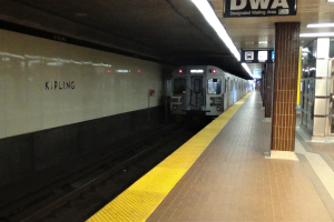 Eine U-Bahn, die in einen Bahnhof einfährt, mit einem Bahnsteig auf der rechten Seite und einem Textschild oben auf dem Bahnsteig.