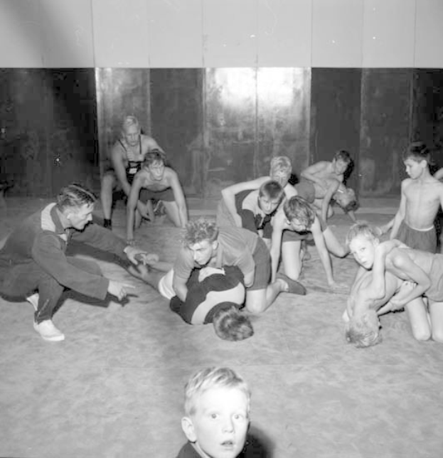 Schwarz-weißes Bild von jungen Jungs, die in einer Turnhalle ringen, mit einer Wand im Hintergrund.
