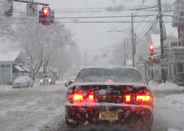 Eine ruhige, schneebedeckte Straße mit Häusern und Bäumen und wenig Verkehr.