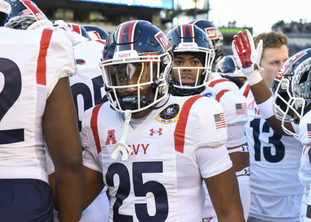 Gruppe von Männern in Football-Uniformen auf einem Feld mit einer unscharfen Menge, Anzeigetafel mit 'Auburn vs Virginia Tech - 11/28/15 College Football Pick, Odds, and Prediction' und Himmel im Hintergrund.