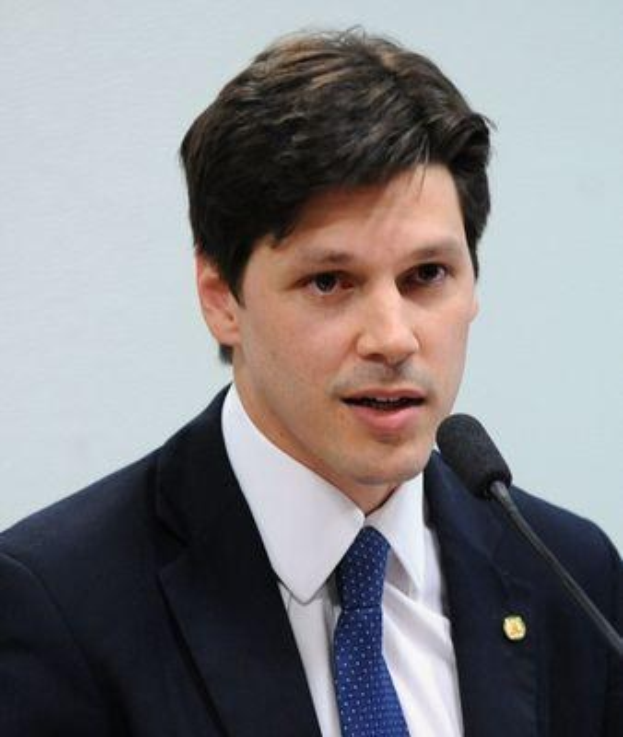 Ein Mann in Anzug und Krawatte spricht in ein Mikrofon vor einer Wand, wahrscheinlich um die Genehmigung eines Gesetzes durch die Regierung zu kommentieren.