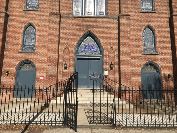 Außenansicht der Ersten Vereinigten Evangelischen Kirche in Chicago, mit einem großen Backsteingebäude, einem schwarzen Tor, Fenstern, Türen, Treppen, Geländern, Lampen und einer Straße im Vordergrund.