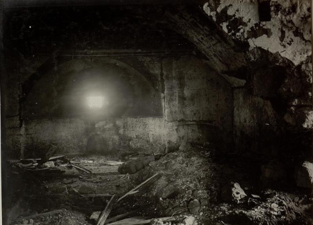 Schwarzes und weißes Foto eines zerfallenden Tunnels in den Berliner Mauertrümmern mit Schutt auf dem Boden und einem Licht am Ende.