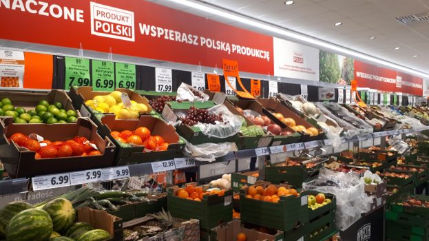 Ladeninneres mit verschiedenen Obst- und Gemüsesorten in Kartons mit Preisschildern und informativen Schildern an den Wänden und Deckenbeleuchtung.