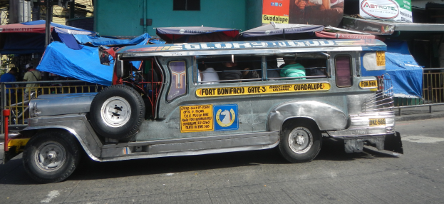 Ein Jeepney ist auf der Seite der Stra├če vor einem Geb├Ąude geparkt, mit Menschen, die darin sitzen, und verschiedenen Gegenst├Ąnden, darunter Zelte, Gel├Ąnder, St├Ąbe und Bretter mit Text und Bildern, im Hintergrund.