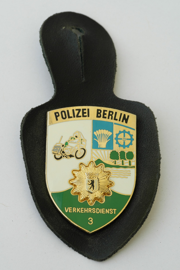 Ein schildförmiges Polizeibadgebzeichen mit der Aufschrift 'Polizei Berlin' auf einem blauen Hintergrund, einem weißen Rand und einem zentralen weißen Stern, das auf einer Oberfläche liegt.
