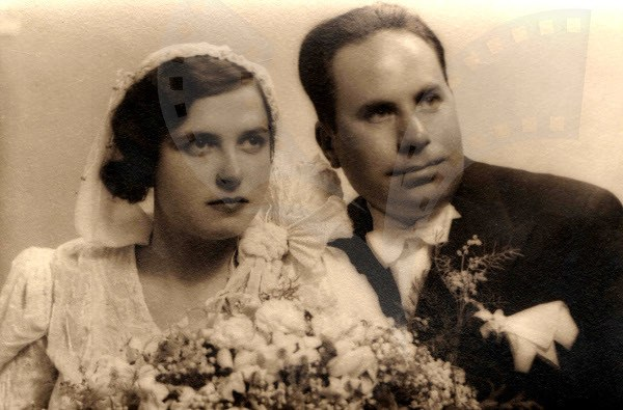 Ein Schwarz-Weiß-Foto eines lachenden Mannes und einer Frau an ihrem Hochzeitstag, die Frau in einem weißen Kleid mit einem Strauß Blumen in der Hand, der Mann neben ihr.