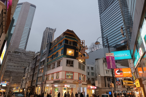 Eine belebte Straße mit hohen Gebäuden, fahrenden Fahrzeugen, Passanten, Bauarbeiten im Vordergrund und sichtbarem Himmel im Hintergrund.