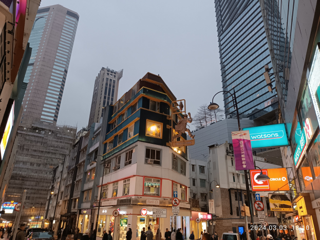 Eine belebte Straße mit hohen Gebäuden, fahrenden Fahrzeugen, Passanten, Bauarbeiten im Vordergrund und sichtbarem Himmel im Hintergrund.